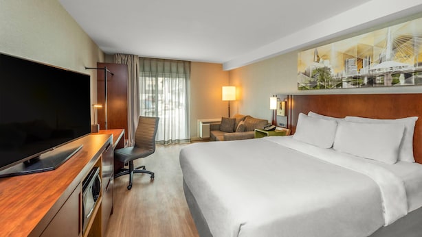 A hotel room with a large bed, a desk with a flat-screen TV, a chair, a sofa, and a painting of a bridge. - Comfort Inn Winnipeg Airport (Winnipeg)