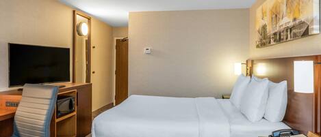 Une chambre d’hôtel comprenant un lit, un bureau avec une télévision, une chaise, une table de chevet avec un téléphone et un tableau accroché au mur.