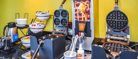 Una estación de gofres con varias planchas para gofres, una máquina para hacer gofres y un dispensador de masa para gofres.