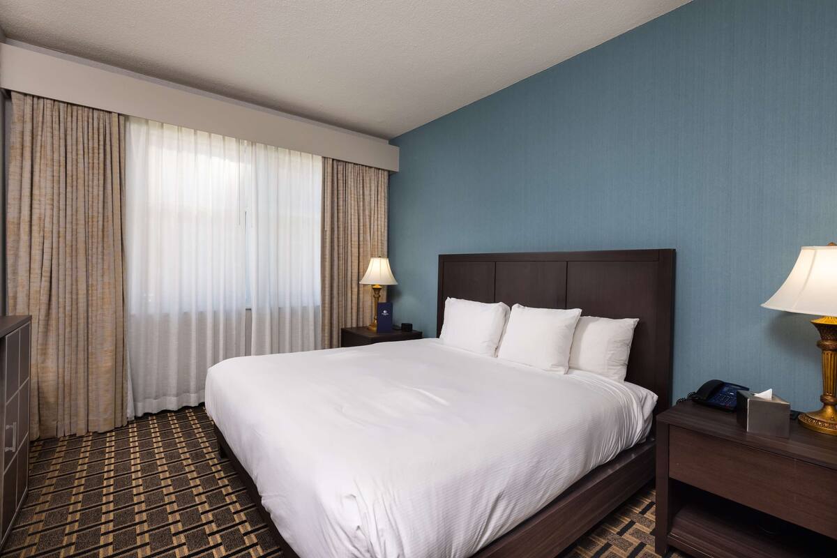 A hotel room with a large bed, two bedside tables, a lamp, and a wardrobe.