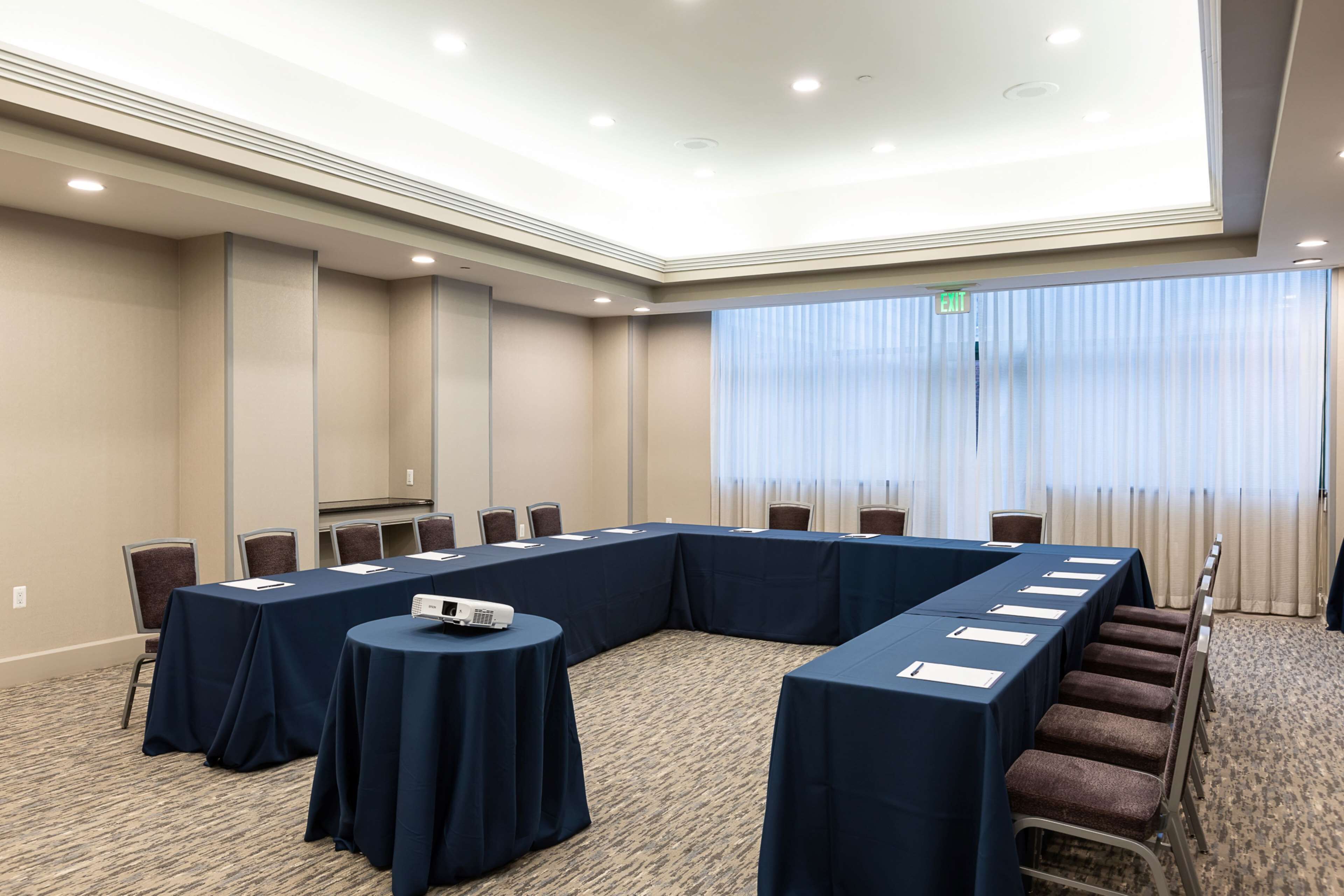 Un salón de conferencias con una larga mesa, sillas, un proyector y suelo alfombrado.