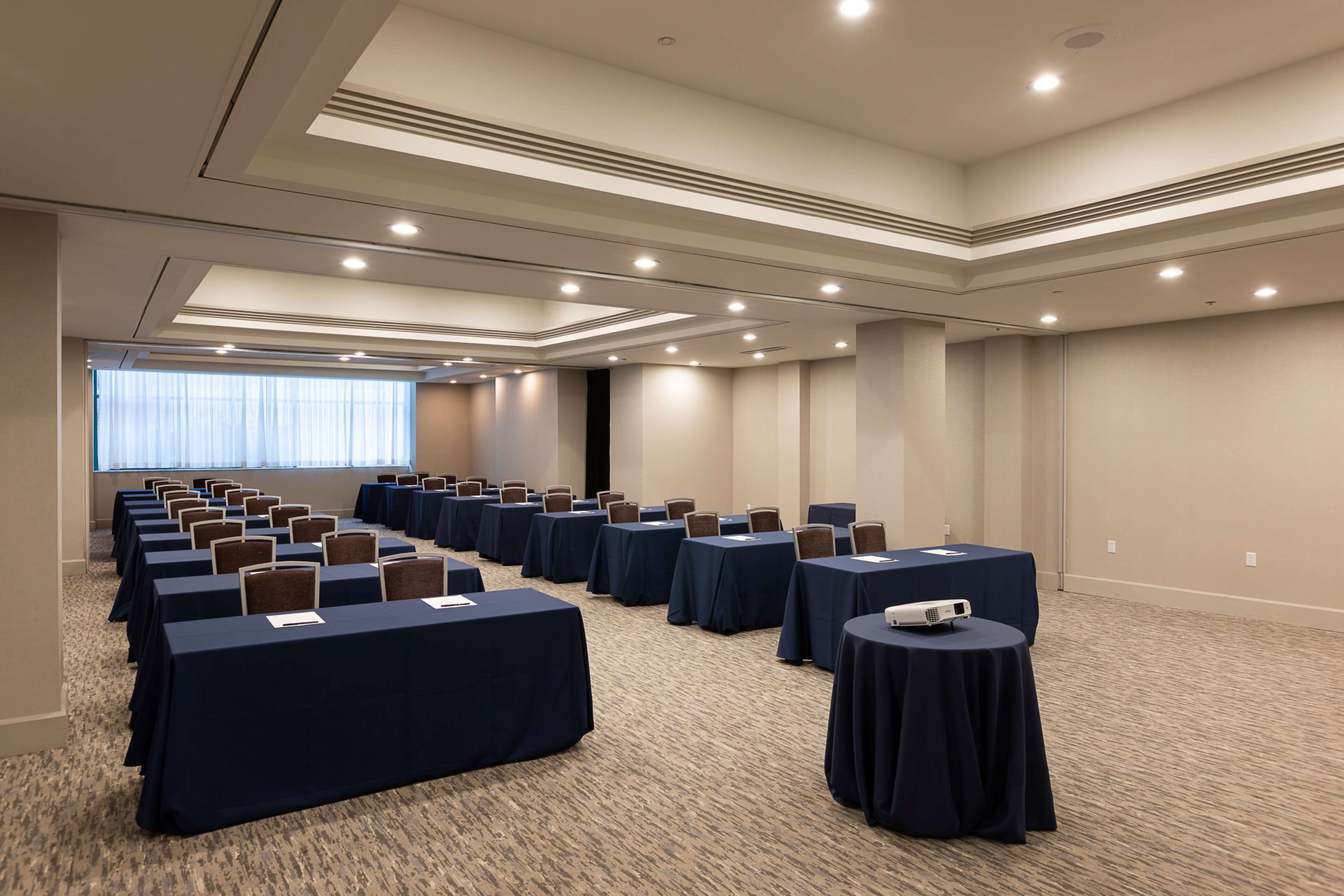 A conference room with rows of tables and chairs, a projector, and a carpeted floor.