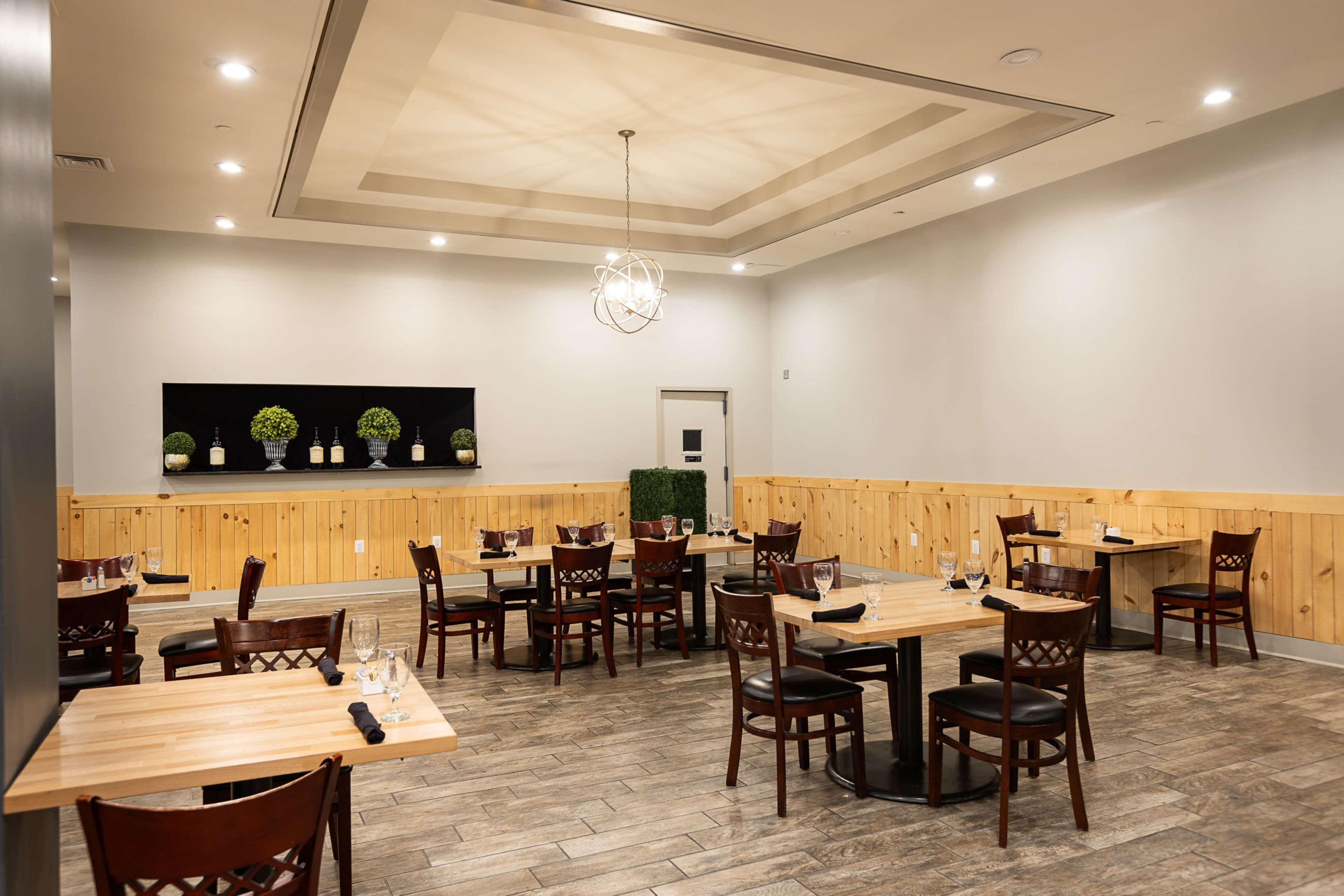 A spacious dining area with wooden tables and chairs, a central chandelier, and a wall-mounted plant display.