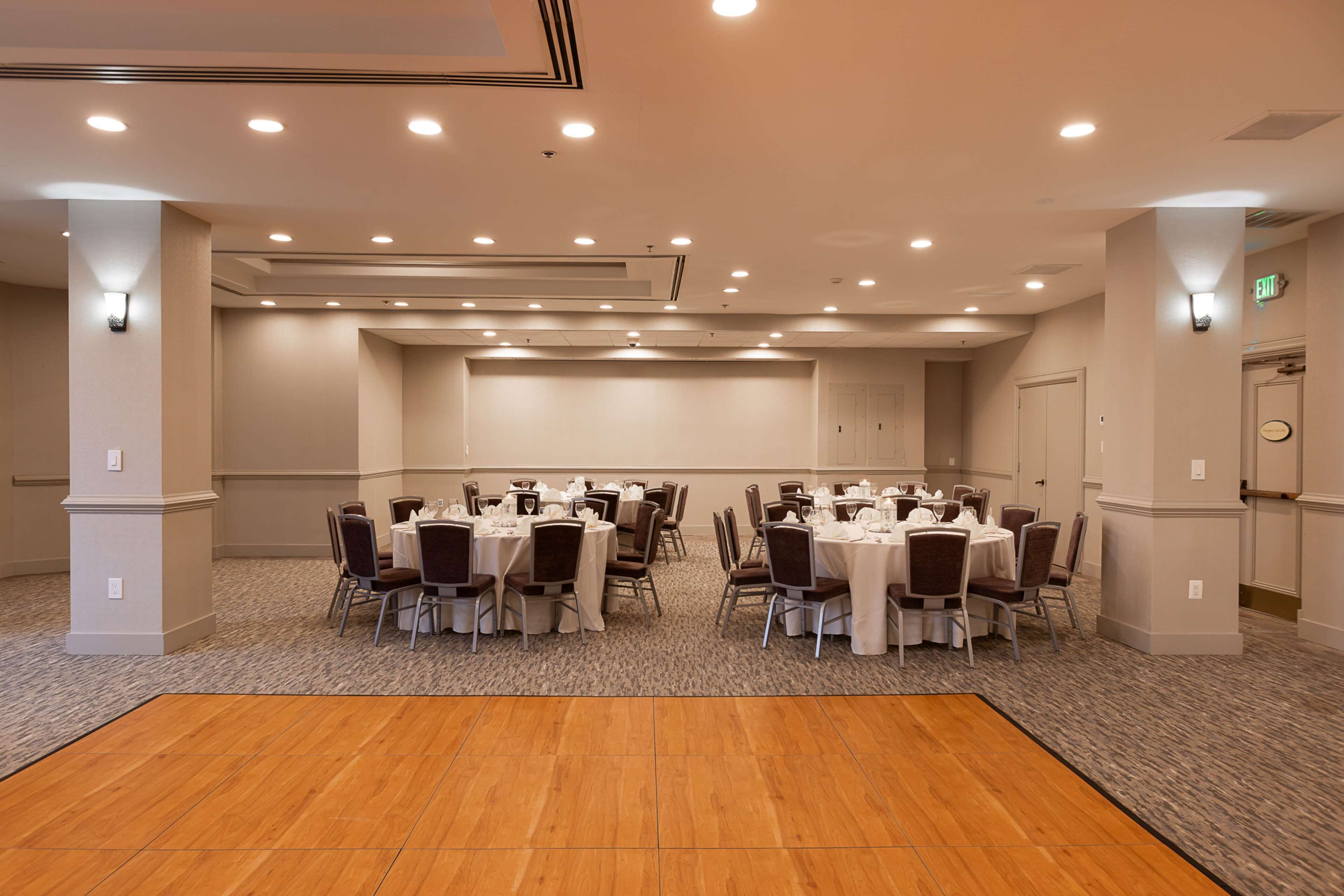 A conference room with round tables, chairs, and a wooden dance floor.