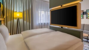 A hotel room with a large bed, a flat-screen TV mounted on the wall, a floor lamp, and a view of the outdoors through sheer curtains. - Spark by Hilton Stuttgart Sindelfingen (Sindelfingen)