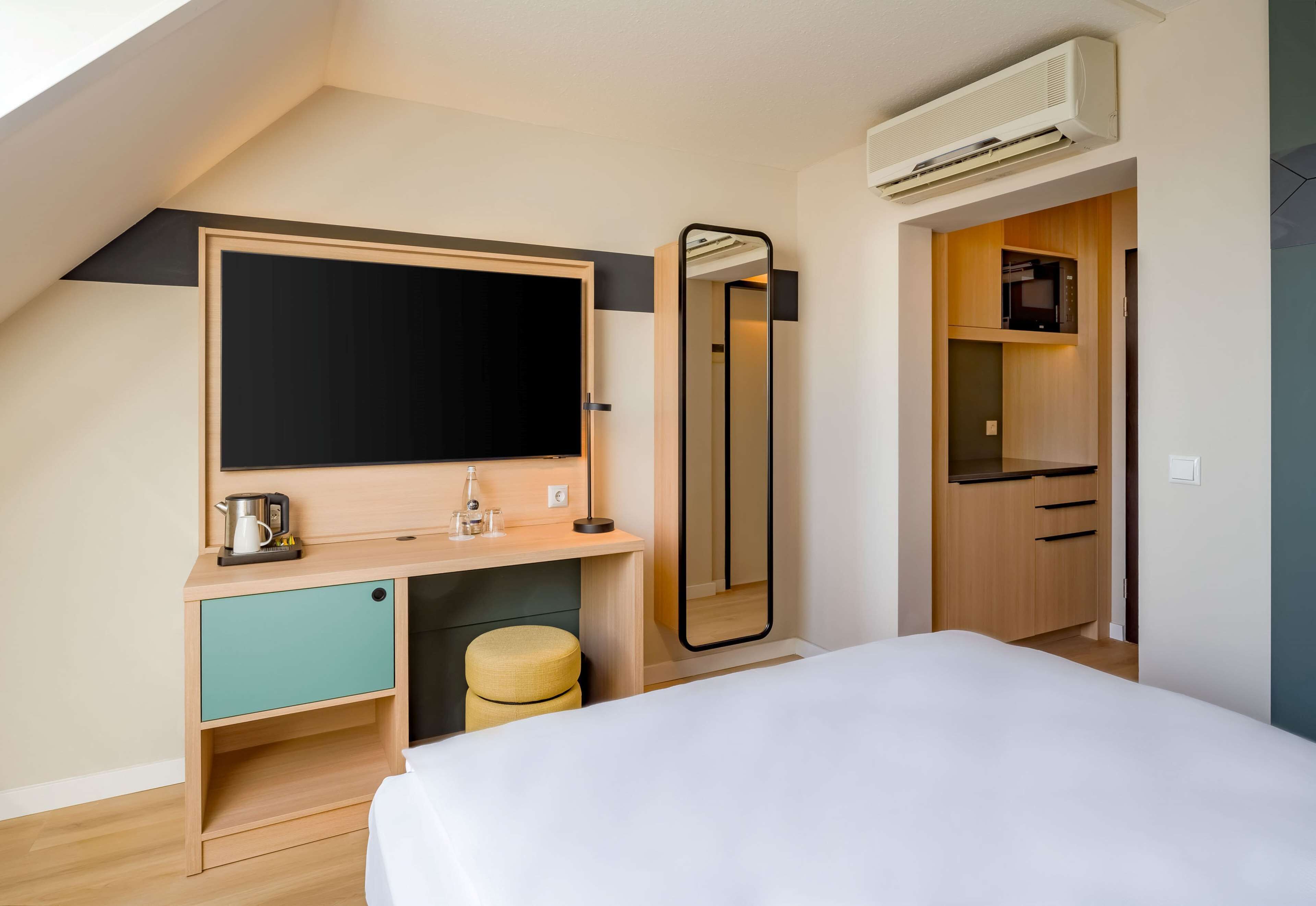 Une chambre à coucher moderne avec un lit, un bureau doté d’un miroir, un petit tabouret et une armoire.