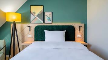Una cama bien hecha con un cabecero verde, una lámpara de noche y dos cuadros en la pared.