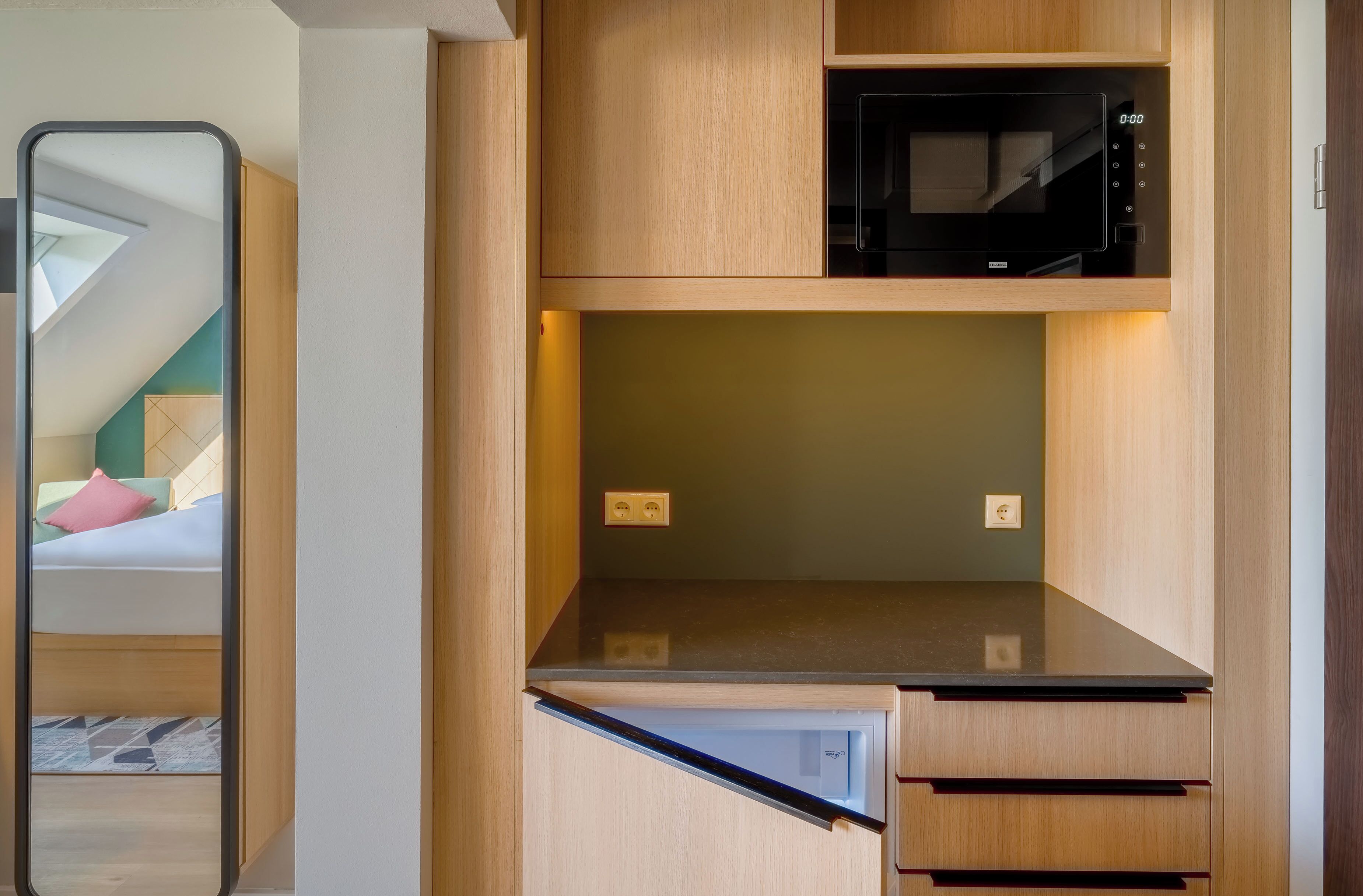 A compact kitchen with a microwave, a small countertop, and wooden cabinetry.