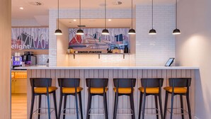 A modern bar area with a white tiled wall, black bar stools with orange cushions, and pendant lighting. - Spark by Hilton Stuttgart Sindelfingen (Sindelfingen)