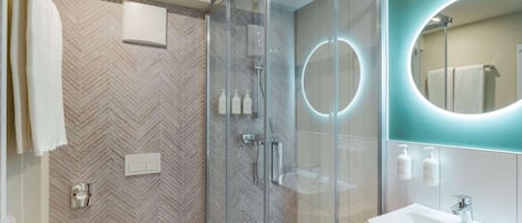 A modern bathroom with a glass-enclosed shower, a large mirror with a circular light, and a white sink.