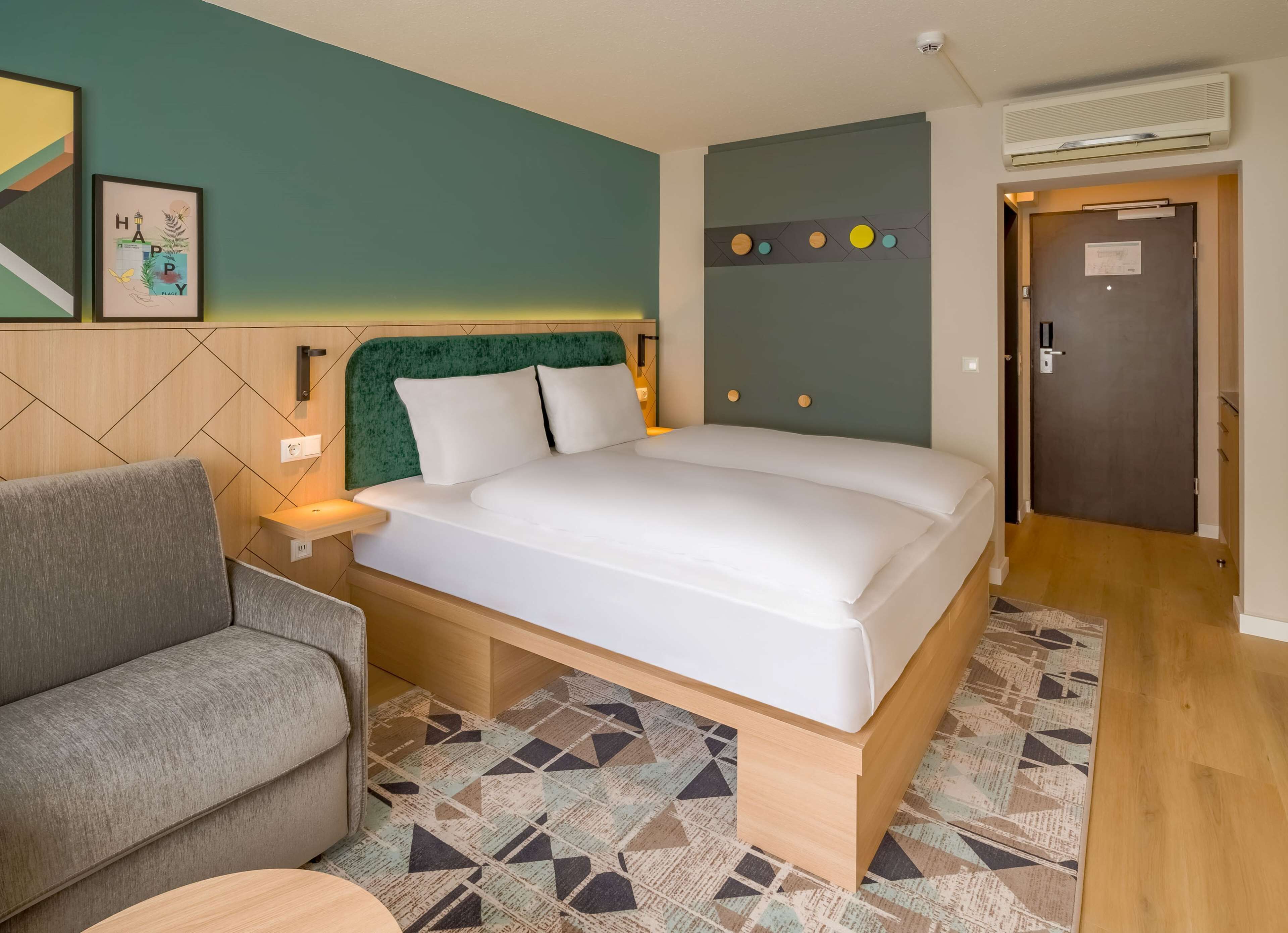 A neatly arranged hotel room with a bed, a sofa, a patterned rug, and a door.