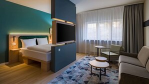 A modern hotel room with a bed, a TV, a sofa, a small table, and a window with curtains. - Spark by Hilton Stuttgart Sindelfingen (Sindelfingen)
