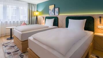 A hotel room with two beds, a small table, a lamp, and a view of the outside.