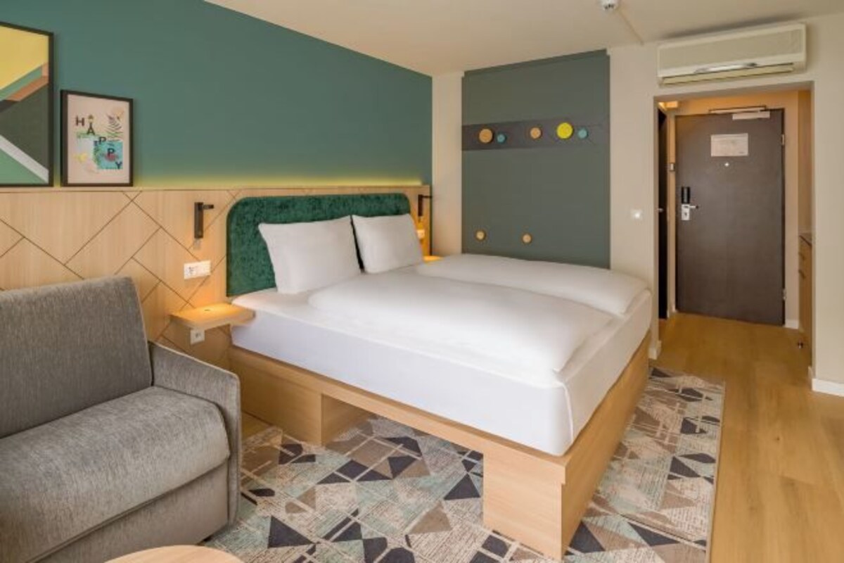 A bedroom with a bed, a sofa, a bedside table, and a wall with artwork.
