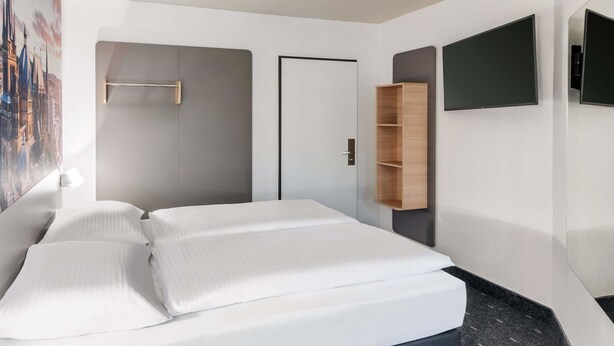 A modern hotel room with a large bed, a wardrobe, a flat-screen TV, and a door. - B&B Hotel Aachen-Hbf (Aachen)