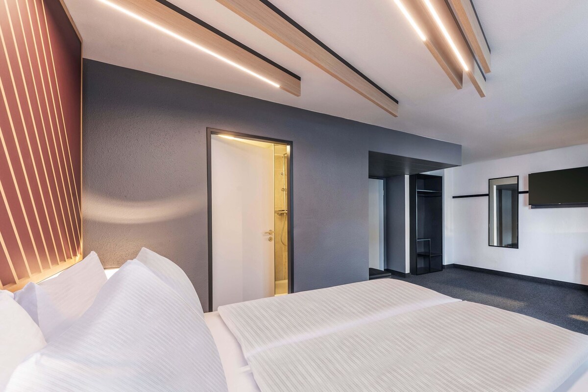 A modern hotel room with a large bed, a walk-in closet, and a shower area.