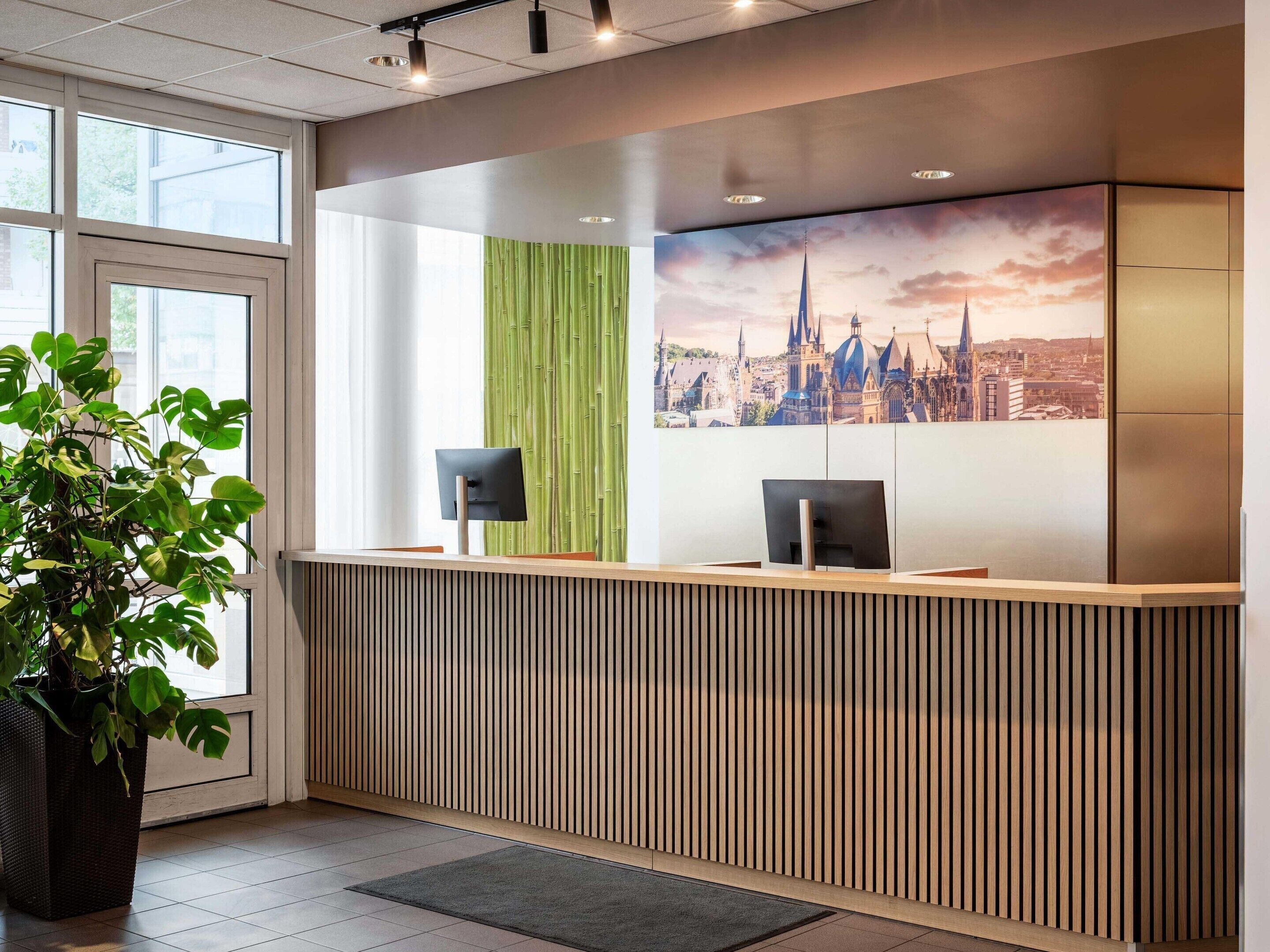 A reception desk with a cityscape mural, a green vertical panel, and a potted plant.