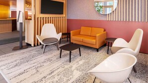 A modern lounge area with a sofa, chairs, a small table, and a television mounted on a wooden wall. - B&B Hotel Aachen-Hbf (Aachen)