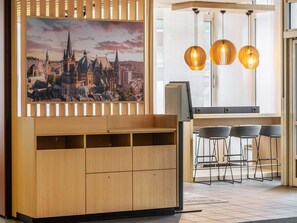 A modern interior with a wooden cabinet, a cityscape painting, and three pendant lights. - B&B Hotel Aachen-Hbf (Aachen)