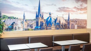 A restaurant with a view of a cityscape, including a church with a spire, a Ferris wheel, and a castle-like building. - B&B Hotel Aachen-Hbf (Aachen)