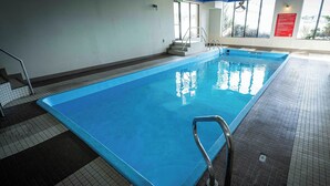 Une piscine intérieure à l’eau d’un bleu limpide, avec un escalier en métal et un revêtement de sol carrelé.