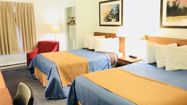 Une chambre d’hôtel avec deux lits, un bureau, une chaise et une fenêtre avec des rideaux.