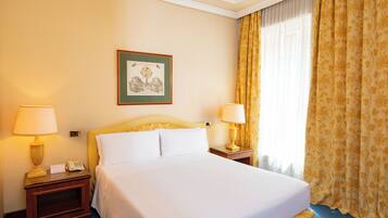 A hotel room with a bed, two bedside tables with lamps, a framed picture on the wall, and a window with curtains.