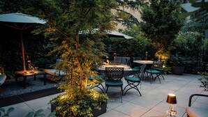Un patio al aire libre con mesas y sillas, rodeado de follaje y árboles.
