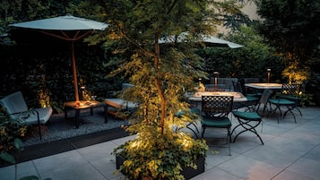 An outdoor patio area with a table and chairs, surrounded by greenery and trees.