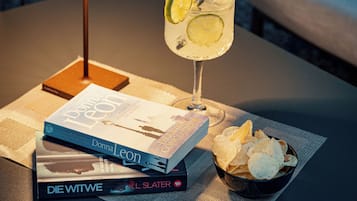 A table with a lamp, a drink with a lemon slice, a bowl of chips, and several books.