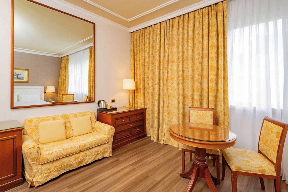 Une chambre d’hôtel équipée d’un canapé, d’une table à manger, d’une chaise, d’une commode et d’un grand miroir.