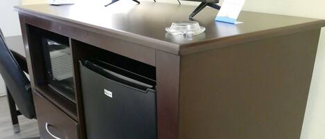 Un bureau compact doté d’un téléviseur à écran plat, d’un petit réfrigérateur et de quelques tiroirs.