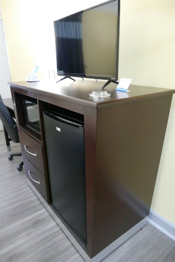 Un bureau compact doté d’un téléviseur à écran plat, d’un petit réfrigérateur et de quelques tiroirs.