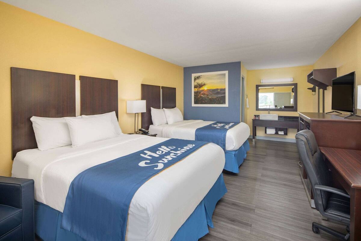 Habitación de hotel con dos camas, un escritorio, una silla, un televisor y un cuadro en la pared.