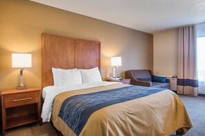 A hotel room with a large bed, bedside tables, a chair, a desk, and a lamp.