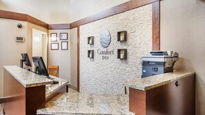 A hotel reception area with a stone wall, a digital clock, framed certificates, and a reception desk with a printer. - Comfort Inn (Bathurst)