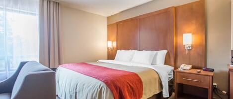 Una habitación de hotel con cama, mesita de noche, lámpara y una silla.