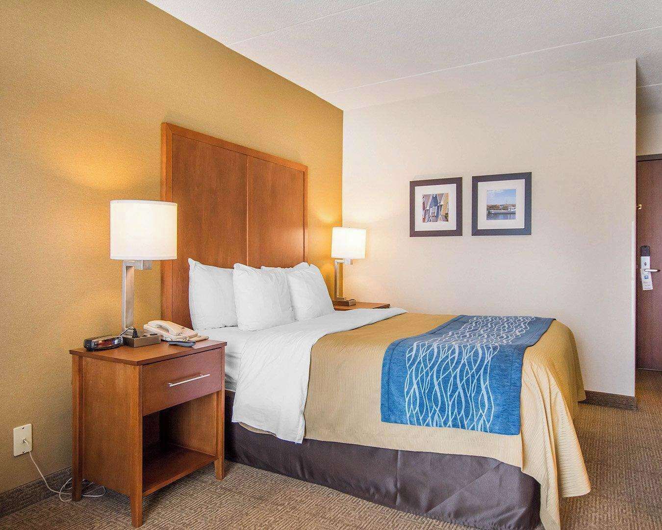 Una habitación de hotel con una cama, dos lámparas de noche, una mesita de noche con un teléfono y un cuadro colgado en la pared.