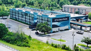 Un bâtiment moderne aux couleurs bleu et blanc, portant l’inscription « The Great Rivers ». On y voit un parking avec plusieurs voitures et, au premier plan, une station-service.