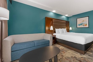Una habitación de hotel con cama, sofá, una mesita y un cuadro en la pared.