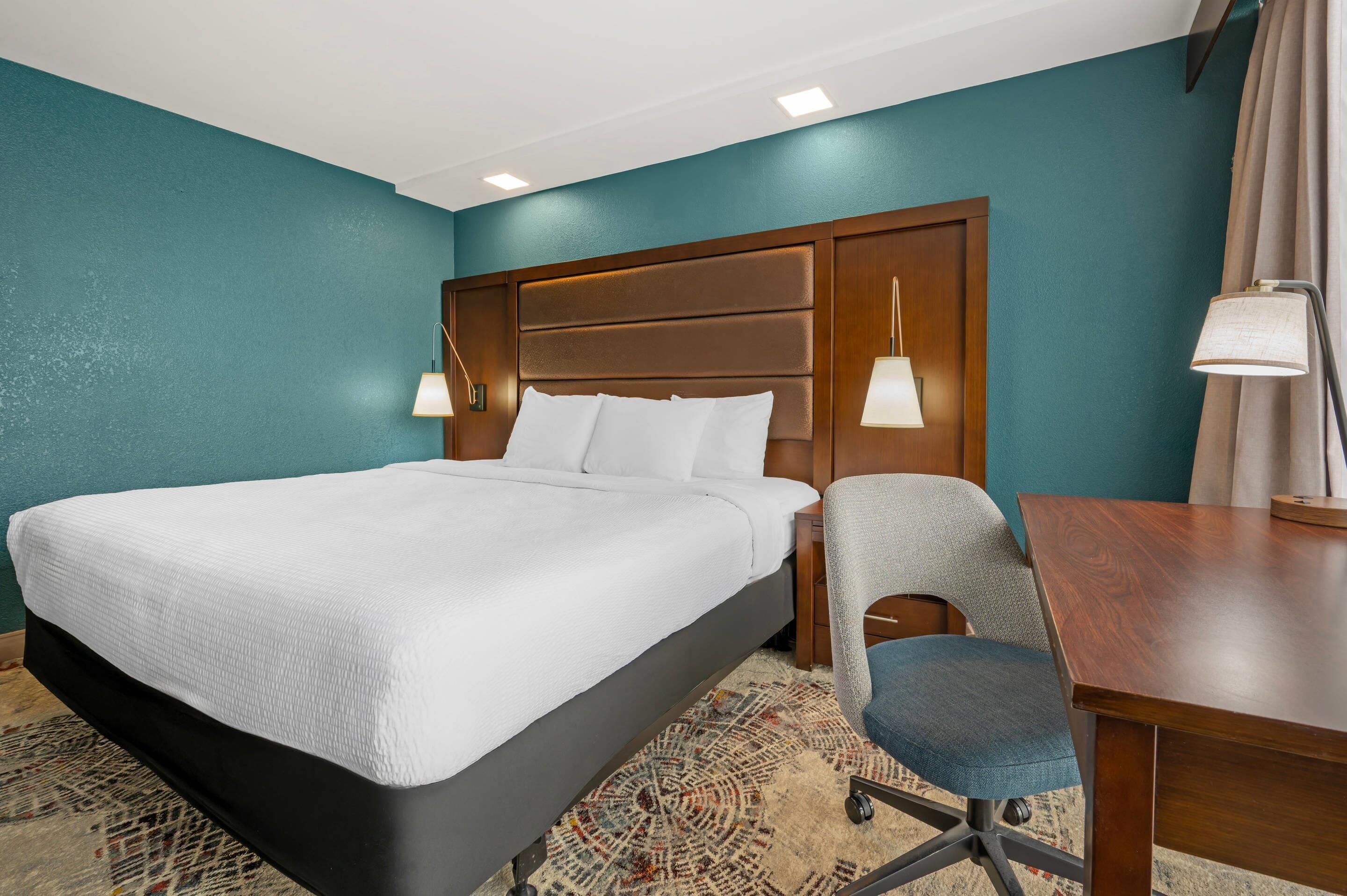 Ein Hotelzimmer mit einem großen Bett, einem Schreibtisch, einem Sessel und zwei Nachttischlampen.