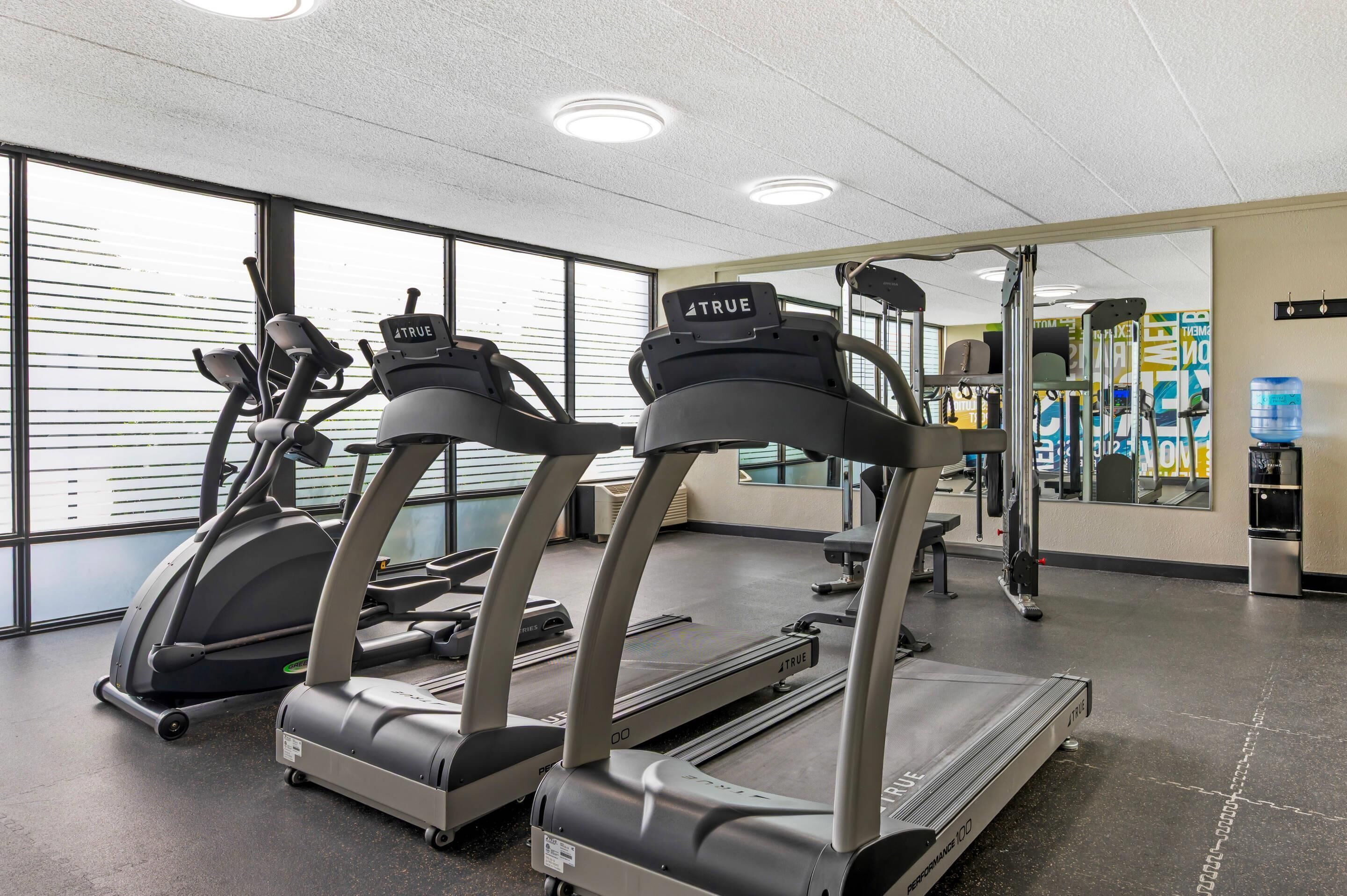 Une salle de sport équipée de tapis de course, d’appareils d’exercice et d’un distributeur d’eau.