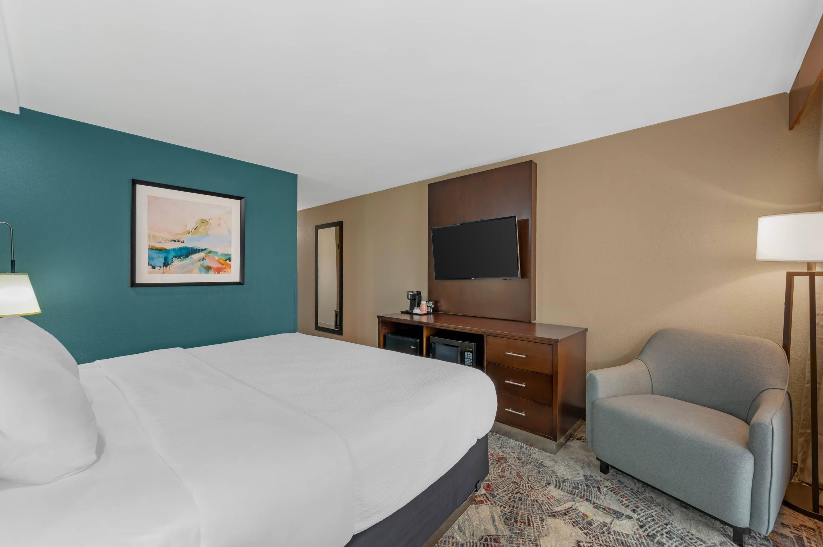 A hotel room with a bed, a desk, a chair, a television, and a painting on the wall.