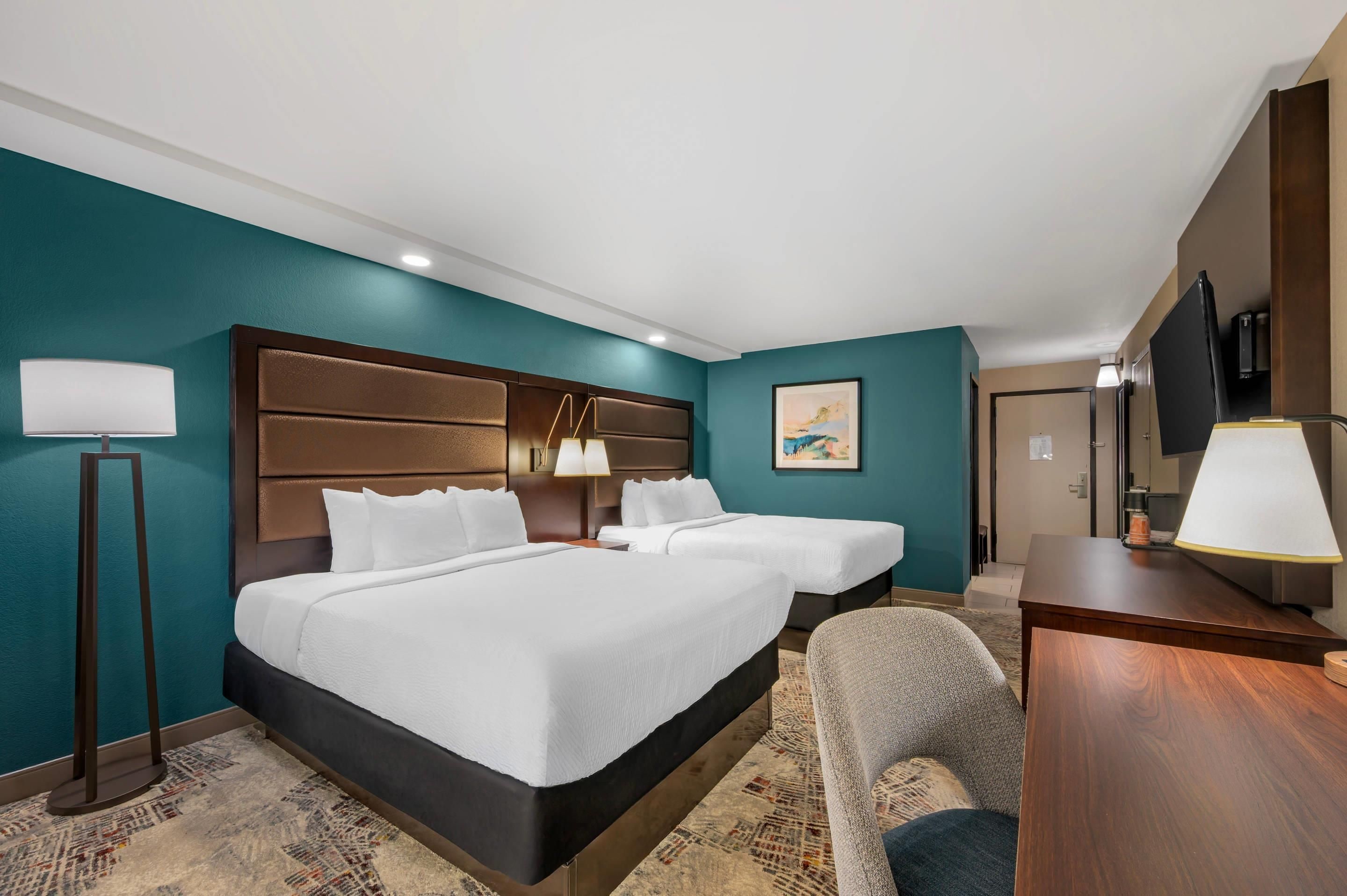 Quarto de hotel com duas camas, uma escrivaninha, uma cadeira e uma televisão.