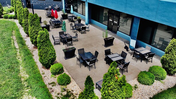 Un espace extérieur aménagé en terrasse, avec plusieurs tables et chaises, entouré d’arbustes soigneusement taillés et d’un chemin de gravier.