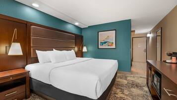 Habitación de hotel con una cama grande, cabecero de madera, dos lámparas de noche, una obra de arte enmarcada en la pared y un escritorio con cafetera.