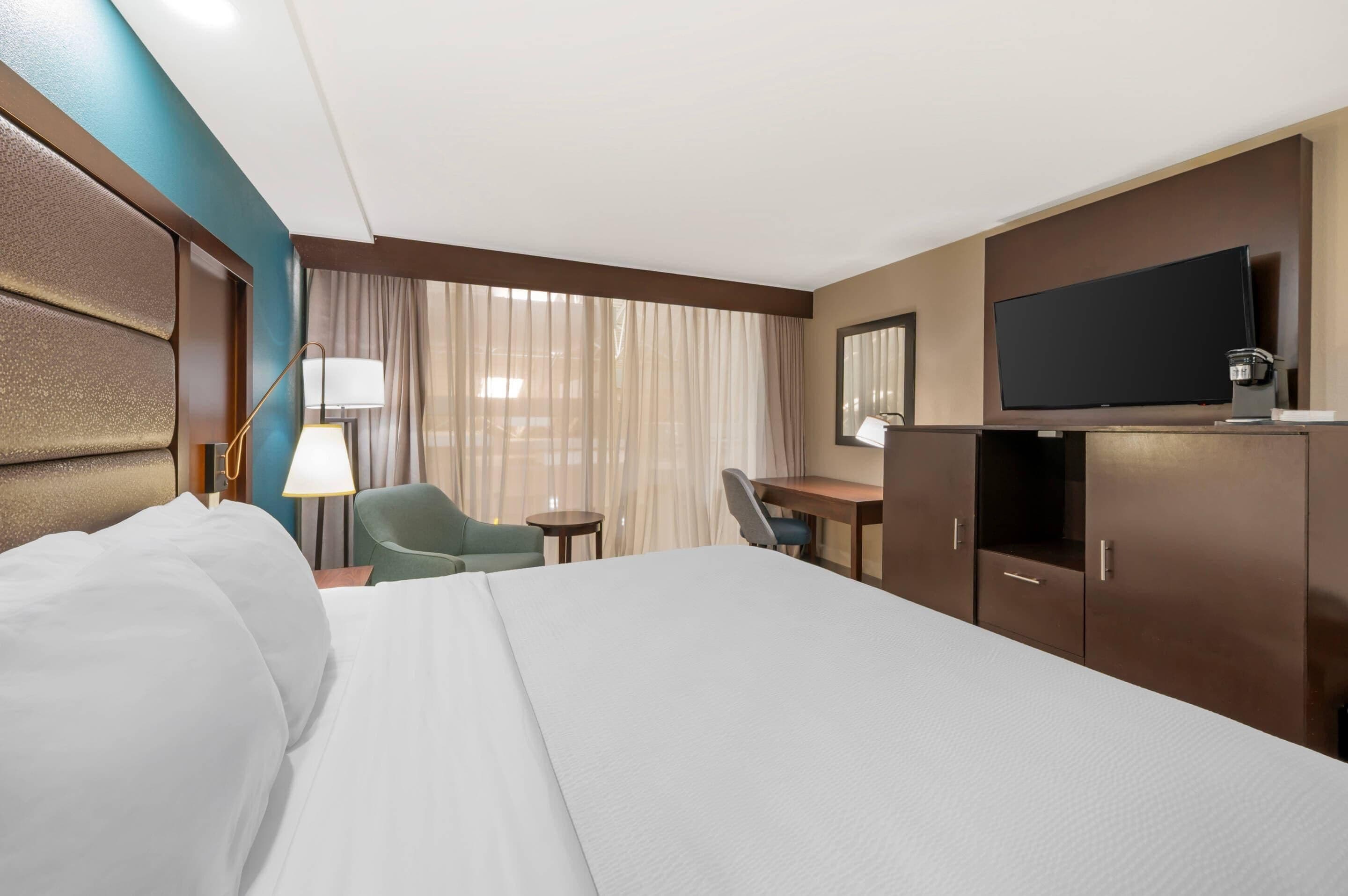 Une chambre d’hôtel équipée d’un lit, d’un bureau, d’une chaise, d’une télévision et d’une fenêtre avec des rideaux.