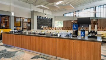 A modern kitchen area with a central island, coffee machines, and a large window providing natural light.