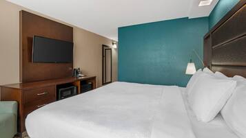 Una camera d'albergo con un letto, una TV a schermo piatto fissata al muro, una scrivania con una macchina del caffè e una lampada.