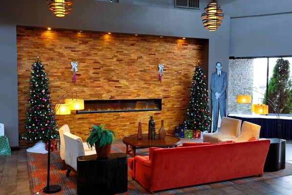Un vestíbulo moderno con una pared de ladrillo, dos árboles de Navidad, una chimenea y una estatua grande.